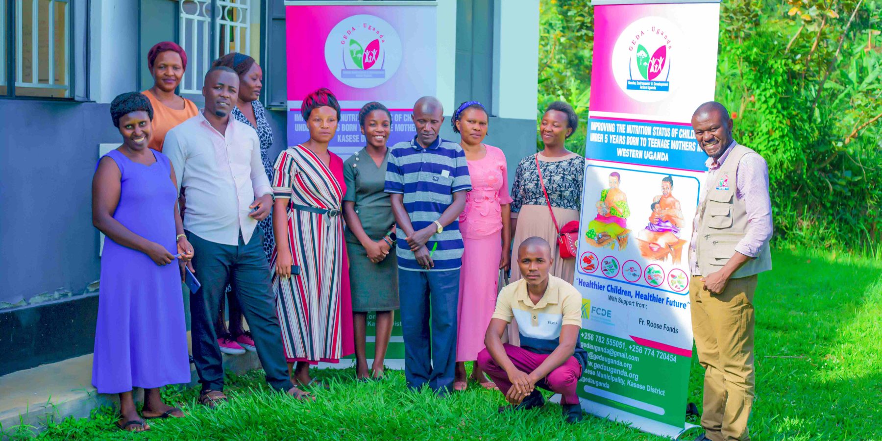 GEDA staff and participants outside a training venue in Kasese, beside project banners