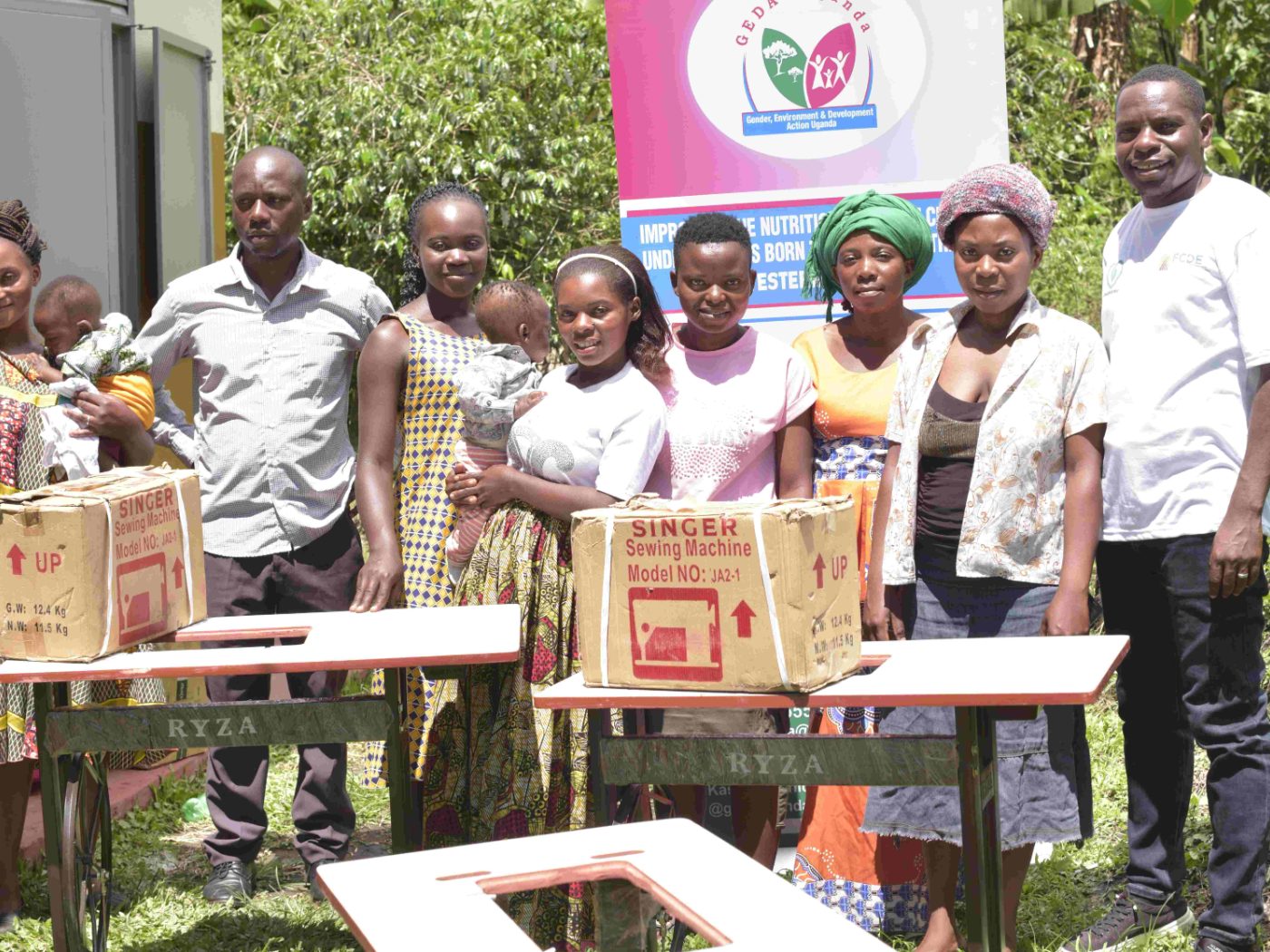Teenage mothers and GEDA staff with newly delivered Singer sewing machines, beneath the project banner